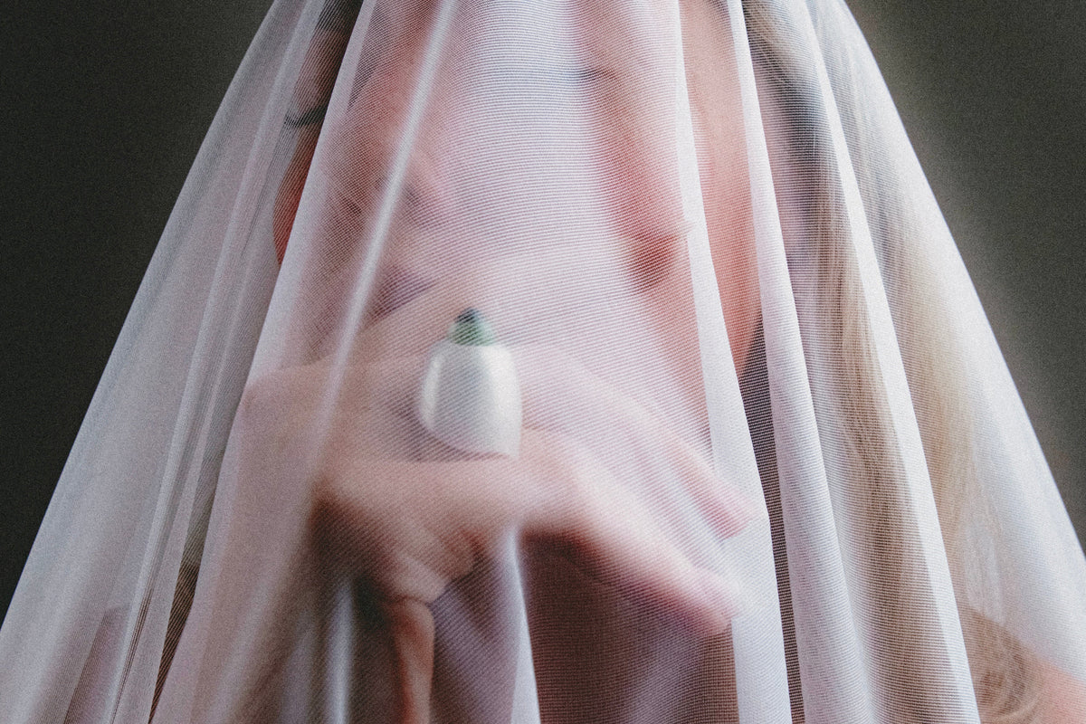 Person holding a white flower behind a sheer fabric against a dark background